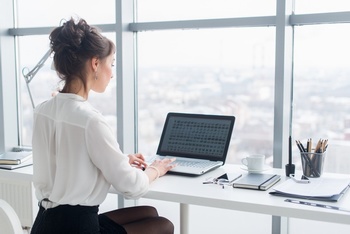 一位女士在窗前的工作台上操作笔记本电脑
